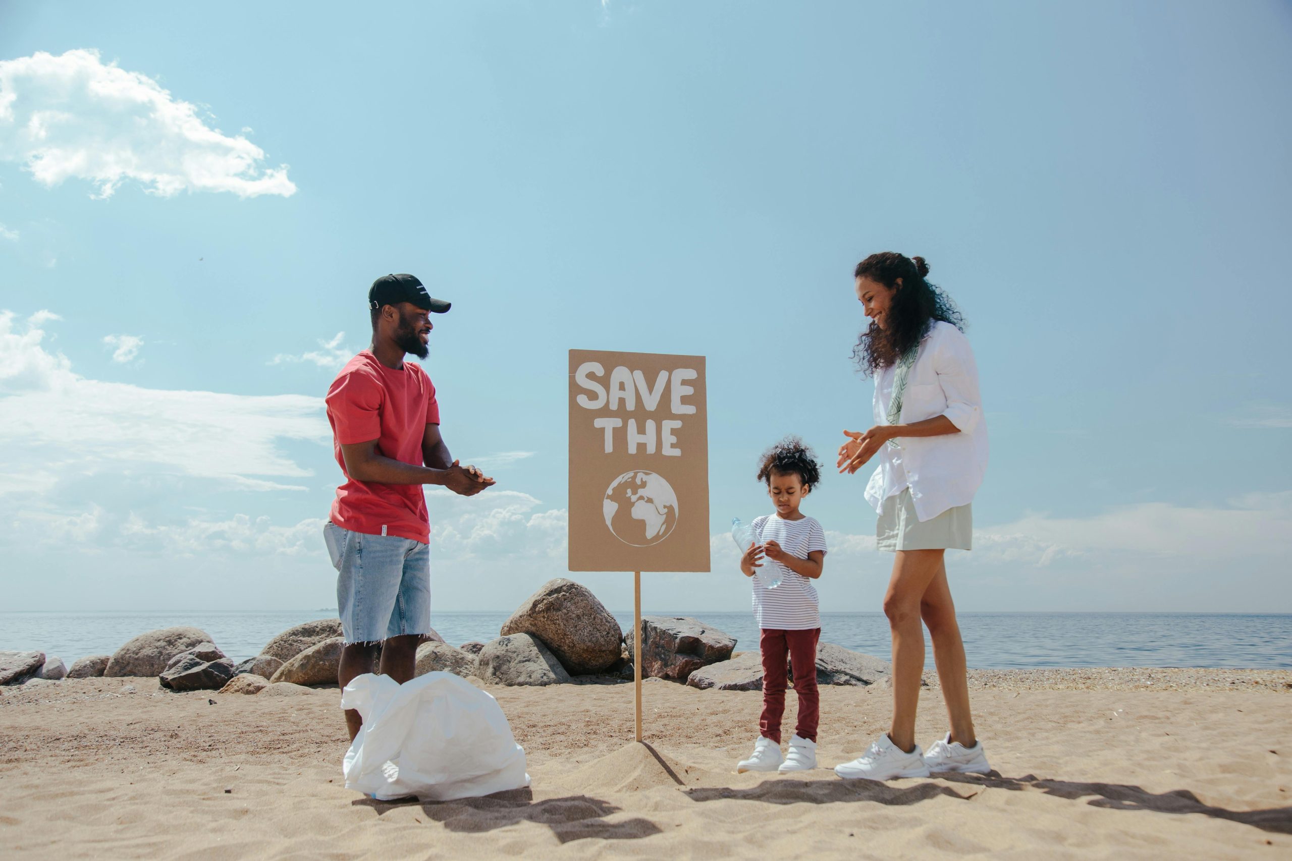 Family participates in beach cleanup with a 'Save the Planet' sign promoting environmental awareness.